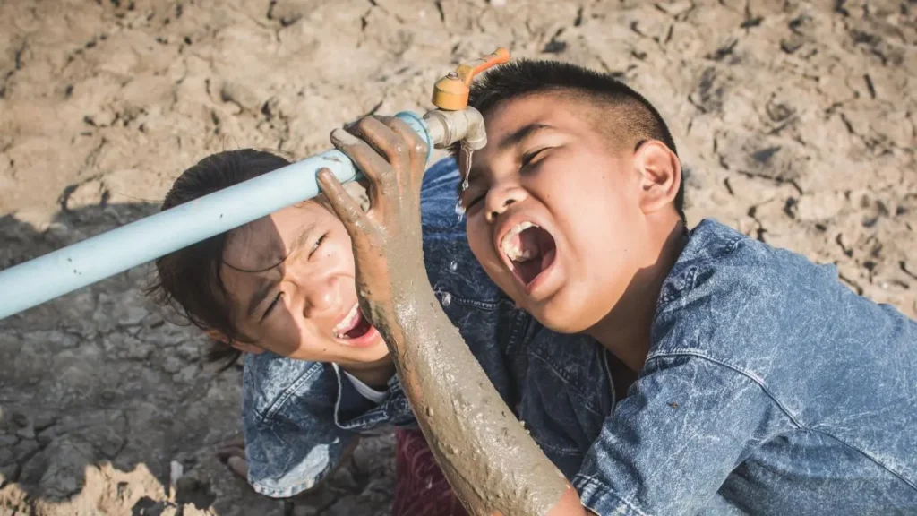2 boys drinking trying to drink water from a tap. 